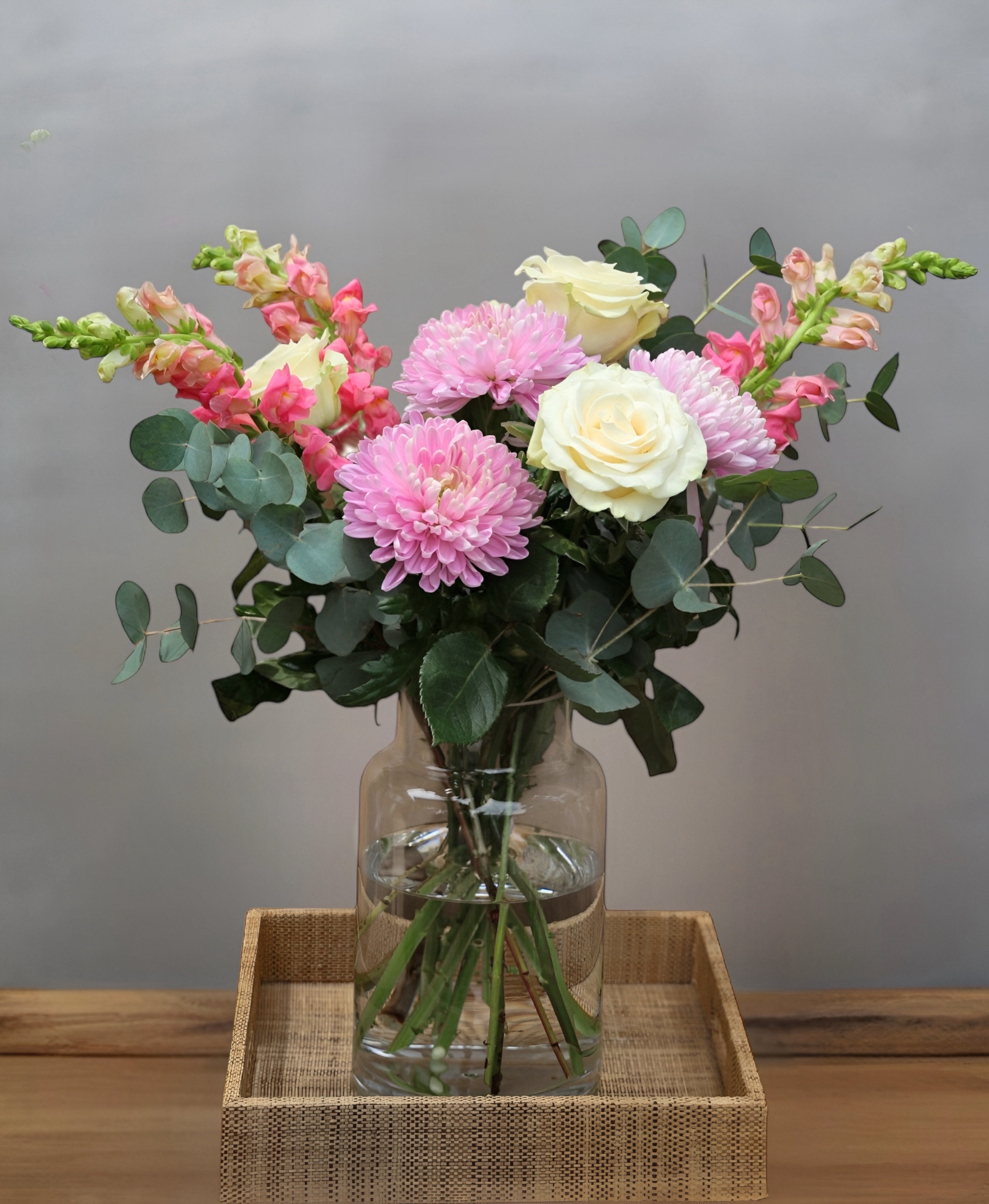 Bouquet of flowers in a clear vase on a wooden tray with a gray background