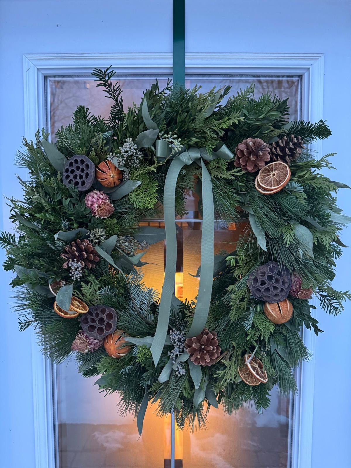 Decorative wreath with greenery, pinecones, and oranges hanging on a door.